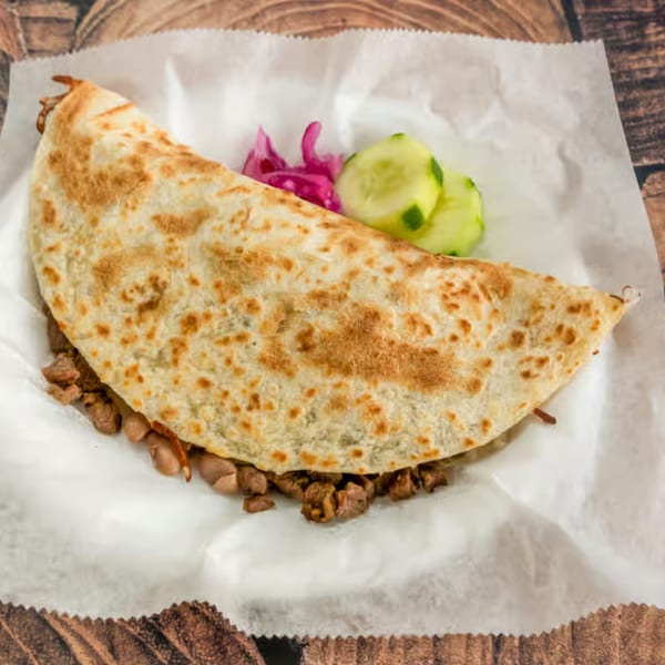 A large El Güero Canelo quesadilla filled with meat and beans, served with pickled onions and cucumbers.