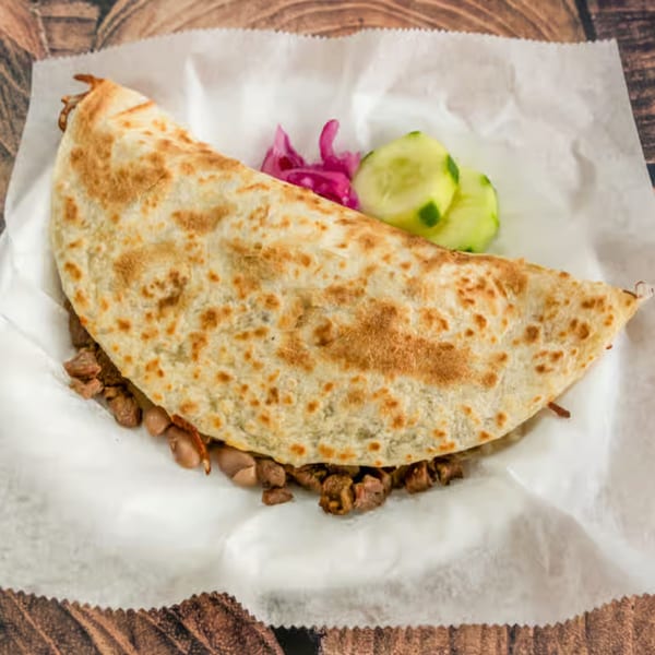 A large El Güero Canelo quesadilla filled with meat and beans, served with pickled onions and cucumbers.