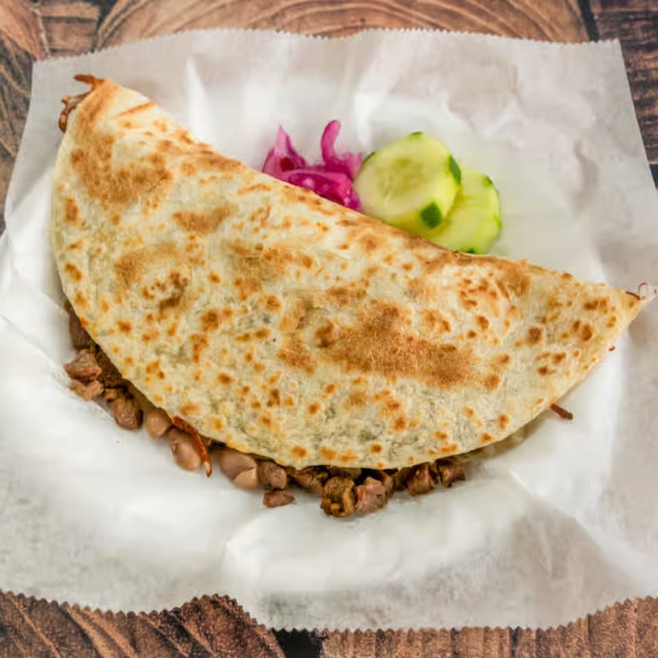 A large El Güero Canelo quesadilla filled with meat and beans, served with pickled onions and cucumbers.