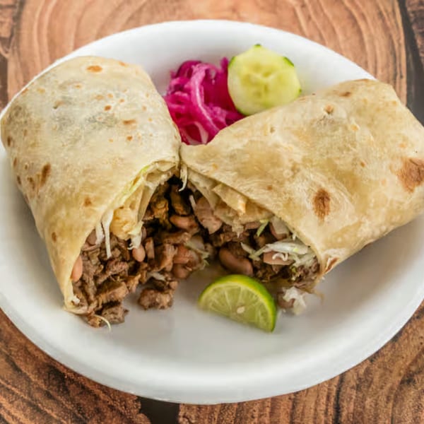 Two carne asada burritos, cut in half, with a side of pickled red onions and lime.